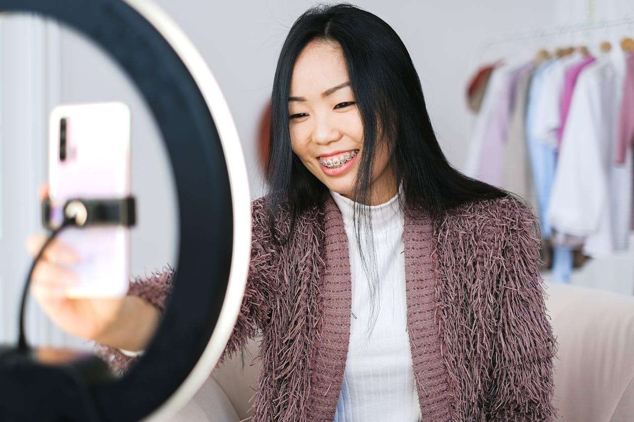 gallery-5 Smiling woman using smartphone and ring light for live streaming indoors.